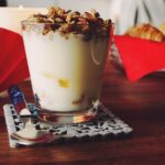 Yogurt greco servito in una ciotola, con frutta fresca e cucchiaio, rappresenta un pasto serale salutare.