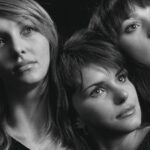 Giocatori sorridenti durante una puntata di Affari Tuoi, con valigette e presentatore sullo sfondo.